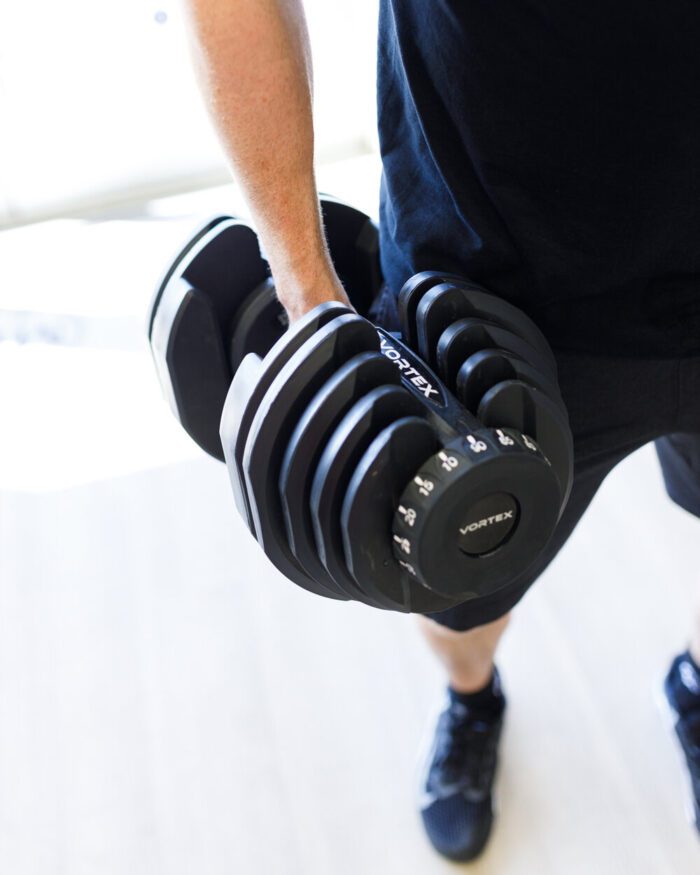 Person lifting adjustable black dumbbell.