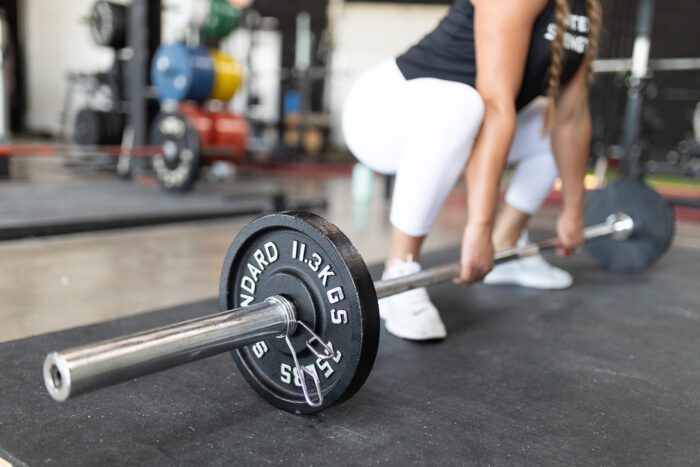 Woman lifting 11.3kg barbell in gym.