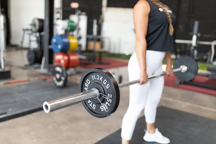 Woman lifting 11.3kg barbell in gym.