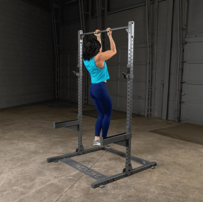 Woman doing pull-ups on a squat rack.