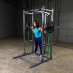 Woman squatting with barbell in a gym rack.
