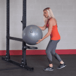 Woman using a gym rack to hold a ball.