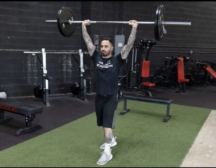 Man lifting barbell overhead in gym.