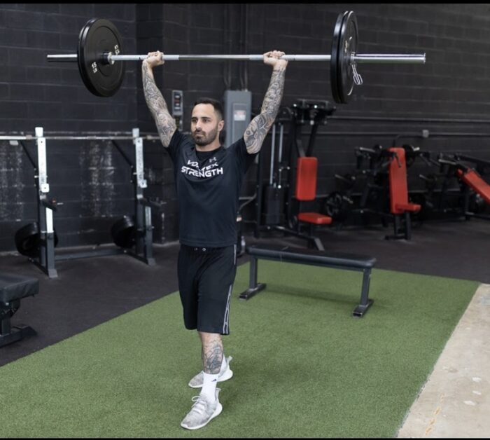 Man lifting barbell overhead in gym.