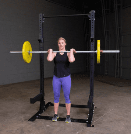 Woman lifting weights in a squat rack.