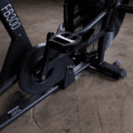 Black stationary bike with fan and pedal.
