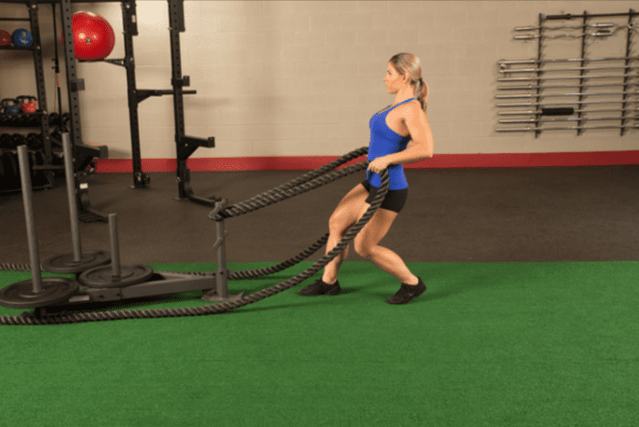 Woman pulling weighted sled with ropes.